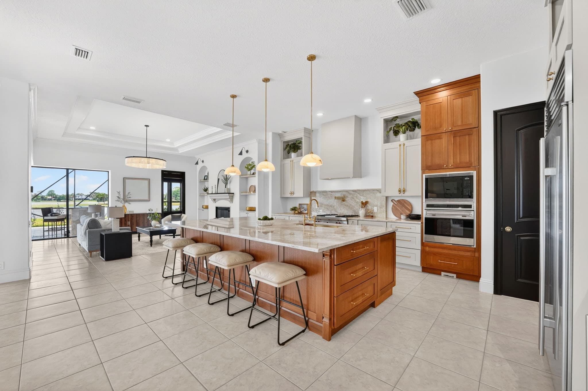 An open-plan kitchen and living area in a PMH listing — marble island, brass pendants, sectional and fireplace beyond, lake visible through the rear windows